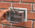 person installing metal box into adapter sleeve on brick wall