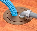 floor box in wooden floor with conduit entering box and bundle of cables exiting box