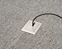 floor box in carpeted floor with device plugged in and routed through slotted cover