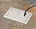 two gang floor box in tiled floor with devices plugged in