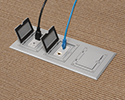 three gang floor box in carpeted floor with devices plugged in