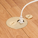Brass floor box with one coin cover off and a wire plugged into the outlet